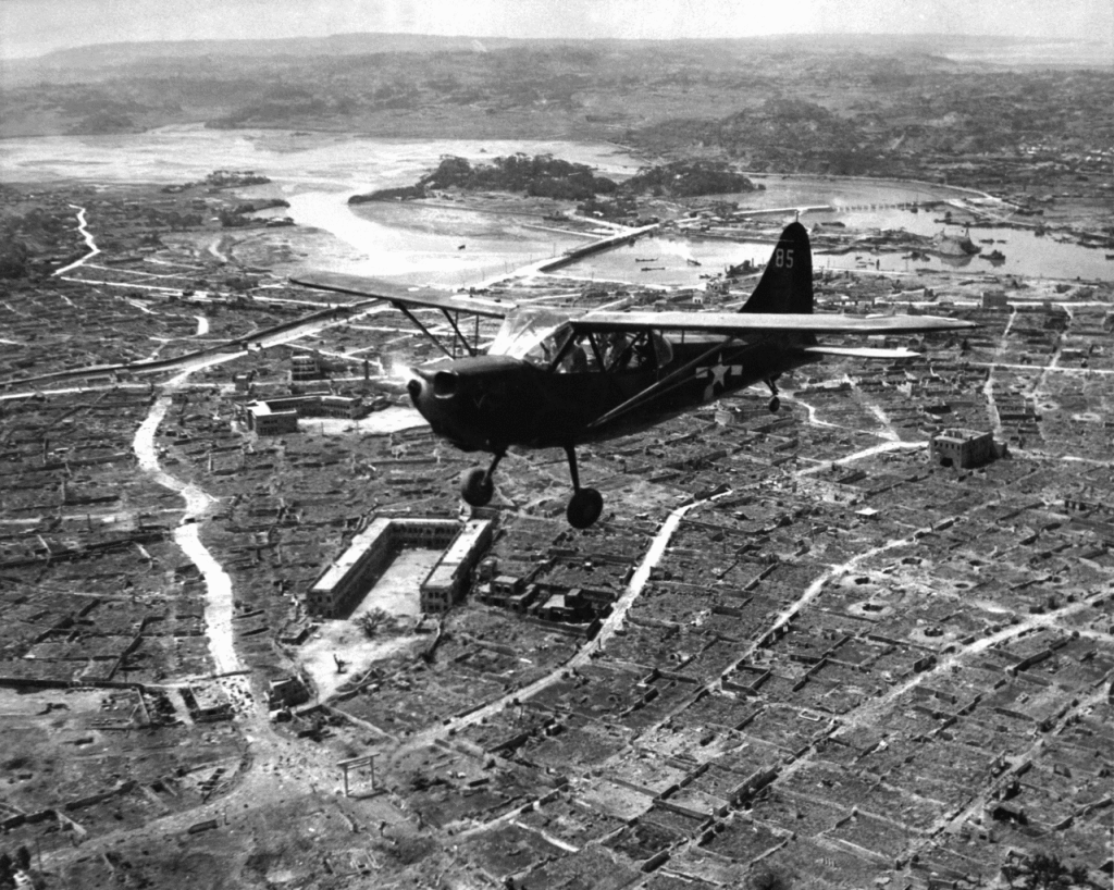 Image of a US Marine Corp observation plane flies over the ruins of Naha, Okinawa.